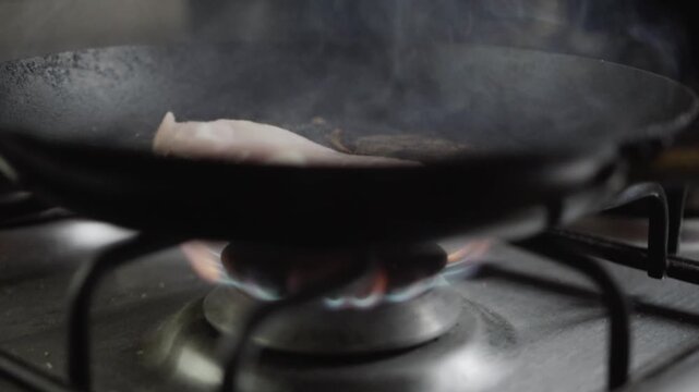 Handheld Slow-Motion Closeup of Raw Pork Chops Being Placed in Black Cast Iron Skillet on Open Flame Gas Stove in Kitchen. Ideal for home cooking videos