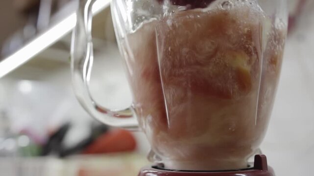 Closeup view of blender mixing tomato pieces into smooth sauce, liquid blending process inside jar, ingredient preparation step for cooking in simple homemade kitchen setup