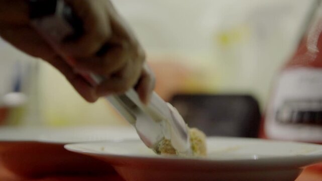 Close view of raw chicken coated in breadcrumbs being dipped into egg mixture with kitchen tools and ingredients blurred in background, highlighting texture and preparation steps