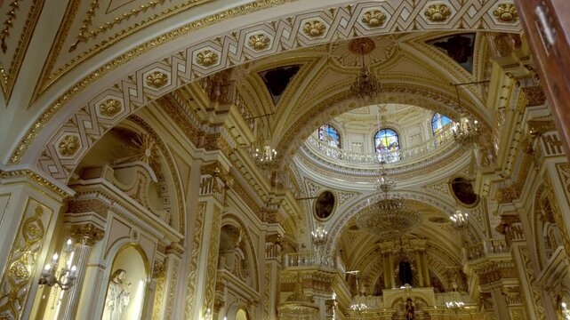 View of ornate church interior with detailed ceiling, chandeliers and arches, rich decoration and symmetry, historic religious architecture in Cholula Puebla captured in soft light
