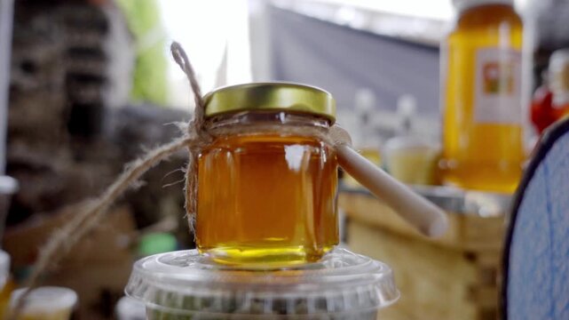 Close view of small glass jar filled with golden honey tied with rustic string and wooden dipper resting on top, warm light highlighting texture and natural sweetness in kitchen setting