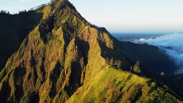 Steep mountain ridge with sharp green slopes in golden hour light across high altitude landscape on Mount Abang Bali with deep shadows and dramatic terrain smooth aerial drone footage