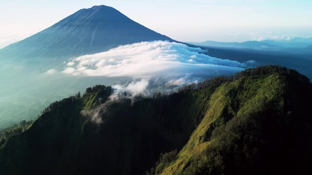 Volcanic mountain with rolling clouds over ridge and steep green slopes in foreground showing dramatic tropical landscape and natural terrain with dynamic weather aerial drone footage