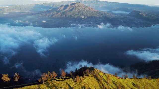Mount Batur volcanic landscape with wide caldera and crater lake with soft clouds over lake in warm golden light across Bali highland terrain with depth and contrast slow descending aerial drone view