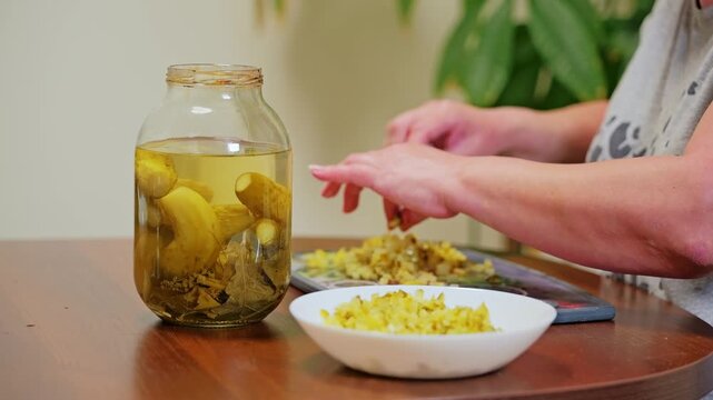 Woman slices pickled cucumbers while reaching into jar creating homemade meal