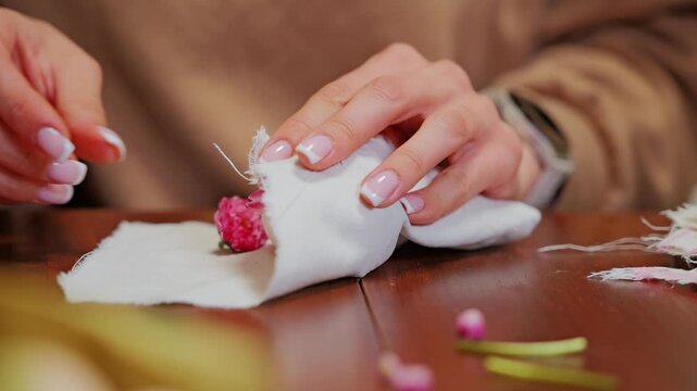 Woman with french manicure wraps tiny blooms onto egg creating festive craft