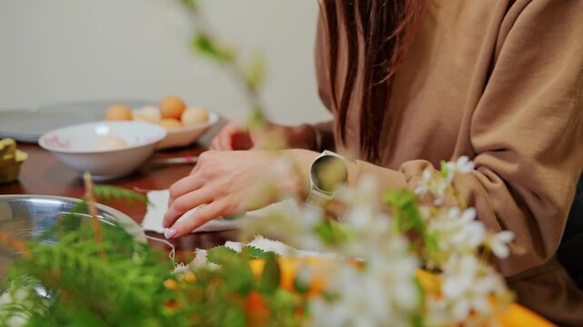 Woman carefully places tiny blossoms on egg preparing natural festive coloring