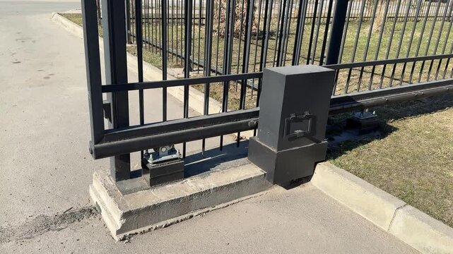 Automatic sliding iron gate, residential entrance, sunny spring day, closeup of lower track and wheel mechanism on asphalt