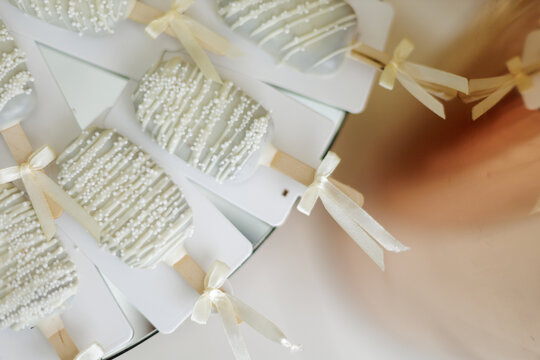 Elegant White Chocolate Cakesicles Decorated with Sugar Sprinkles and Silk Ribbons