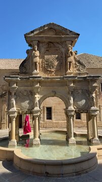 Woman in red dress walking past historic Renaissance fountain in Spain