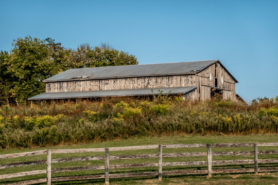  Old Wooden Barn on Rural Farmland with Weathered Structure Grass Field and Fence Under Clear Blue Sky