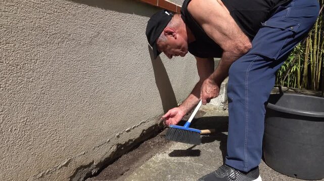 Man uses brush and shovel to clean the ground for flowerbed by wall area