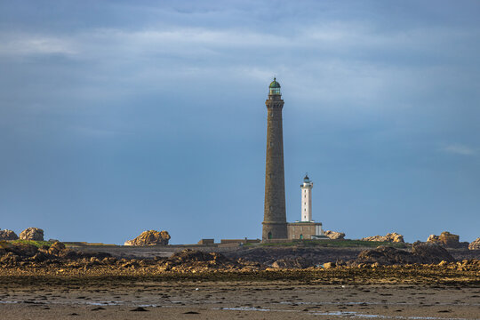 View of the Ile Vierge lighthouse featuring the tall stone tower and adjacent white lighthouse on the rocky coast of Plouguerneau, Bretagne, France.