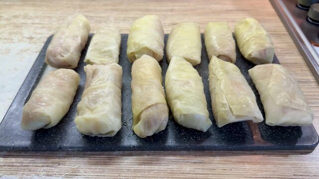 Cabbage rolls on black cutting board closeup, uncooked meat filled cabbage leaves rolled into neat cylinders, arranged in rows