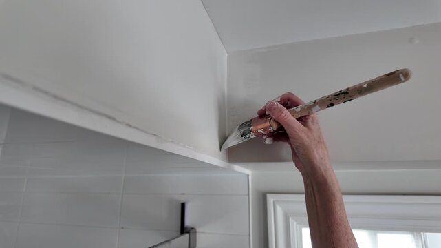 Woman painting trim in bathroom while doing house renovations - close up on hand and paint brush