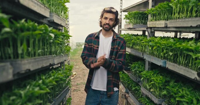 A young man portrair while standing in rows of seedlings in a greenhouse