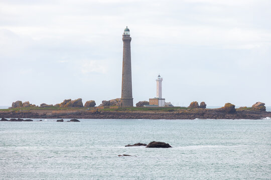 View of the Ile Vierge lighthouse standing tall on a rocky island surrounded by the Atlantic Ocean under a cloudy sky in Plouguerneau, Bretagne, France.