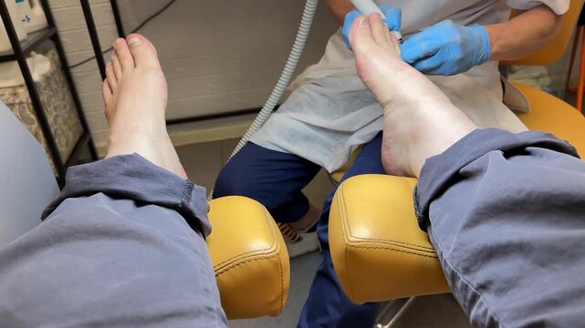 Close-up foot pedicure in beauty salon, master woman pedicurist performs hardware pedicure on male client using diamond cutter bit
