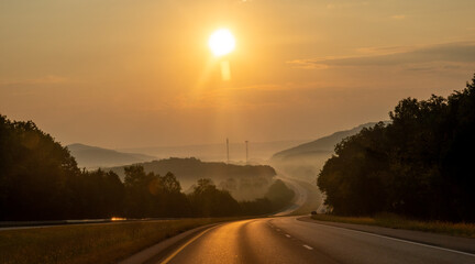 Fototapeta premium Highway Through Misty Mountain Landscape at Sunrise with Golden Light Fog and Rolling Hills Creating Atmospheric Scenic View