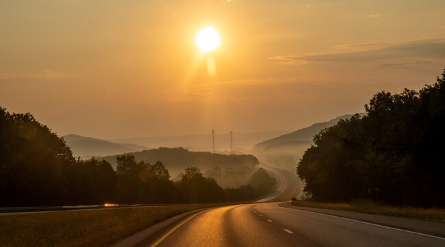 Highway Through Misty Mountain Landscape at Sunrise with Golden Light Fog and Rolling Hills Creating Atmospheric Scenic View