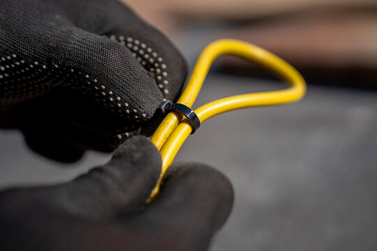 Worker fastens yellow electrical cable loop with black plastic cable tie during outdoor wiring organization and installation.