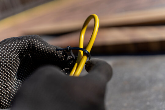Worker fastens yellow electrical cable loop with black plastic cable tie during outdoor wiring organization and installation.