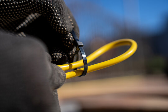 Worker fastens yellow electrical cable loop with black plastic cable tie during outdoor wiring organization and installation.