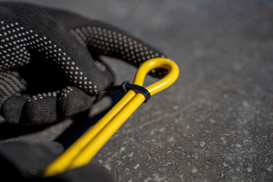 Worker fastens yellow electrical cable loop with black plastic cable tie during outdoor wiring organization and installation.