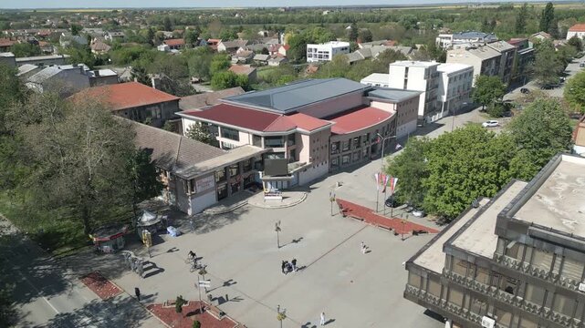 Aerial shot ascending directly over the central town square in Vrbas, Serbia. Focus on the urban plaza layout and surrounding architecture on a bright sunny day.