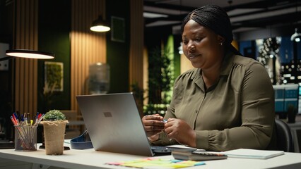 Fototapeta premium African american woman in office chatting on video call and smiling, attentiveness and professionalism. Employee engaging in a virtual conversation, exchanging ideas with associates. Camera A.