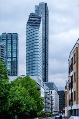 Obraz premium Modern Residential Tower Rising Above Quiet Tree Lined Street in London England Urban Neighborhood Setting