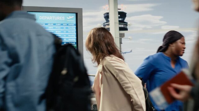 Woman in crowded airport annoyed by flight delay during international holidays season. Tourist looking at boarding gate number on screen in busy transportation hub to catch plane, going home, camera A