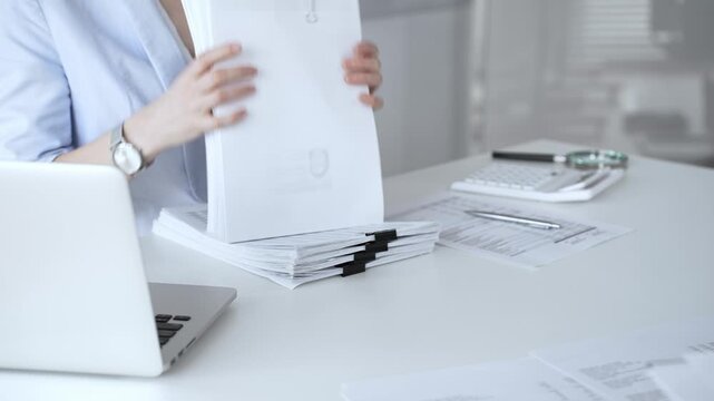 Business person working on financial documents, accounting or auditing a large stack of paperwork, managing tax forms and corporate reports with a pen at an office desk. Audit and taxes