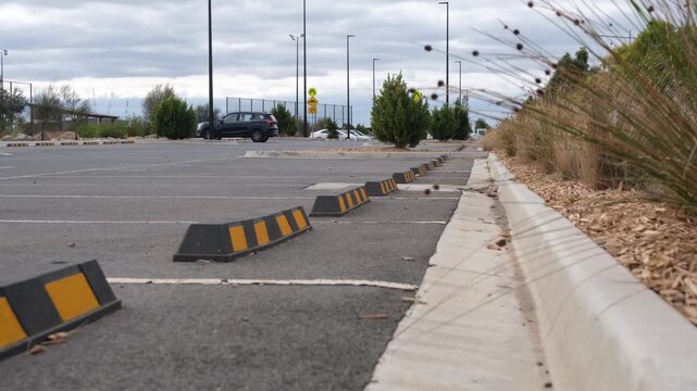 A large outdoor suburban car park featuring safety wheel stops and native grass landscaping. Public infrastructure design and urban land use in Truganina, Melbourne, Australia.