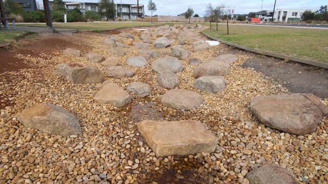 Decorative rock garden and drainage swale in a contemporary Australian neighborhood. Urban stormwater management system using river stones and boulders in parkland. Truganina, Melbourne Australia