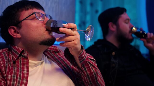 Quiet night spent savoring red wine. Serene evening with friends thad drink alcohol in living room. Relaxation of caucasian man in glasses and plaid shirt that holds glass in hand and enjoys beverage