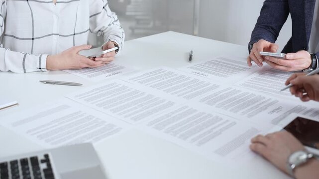 Business people collaborating on contracts and agreements during an important boardroom meeting, navigating legal documents and using mobile phones for quick communication and data access