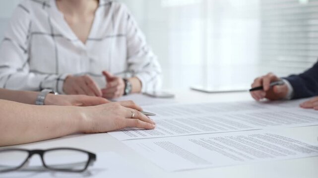 Business professionals reviewing contract documents and discussing terms during a corporate meeting, focusing on agreement details and signature importance for legal finalization