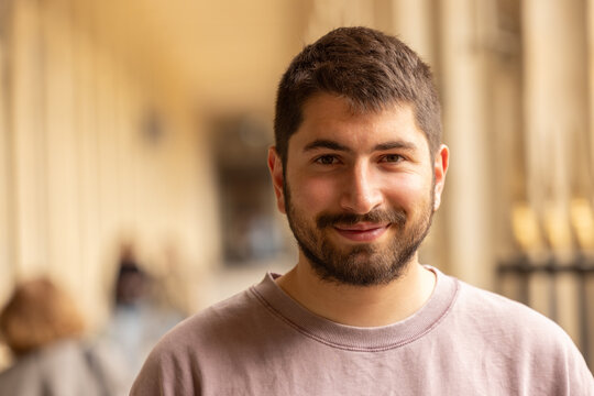 Portrait chaleureux d&rsquo;un jeune homme barbu souriant sous les arcades des jardins du Palais Royal &agrave; Paris avec arri&egrave;re-plan flou
