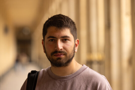 Portrait chaleureux d&rsquo;un jeune homme barbu souriant sous les arcades des jardins du Palais Royal &agrave; Paris avec arri&egrave;re-plan flou
