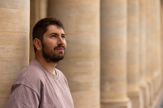 Portrait chaleureux d&rsquo;un jeune homme barbu souriant sous les arcades des jardins du Palais Royal &agrave; Paris avec arri&egrave;re-plan flou