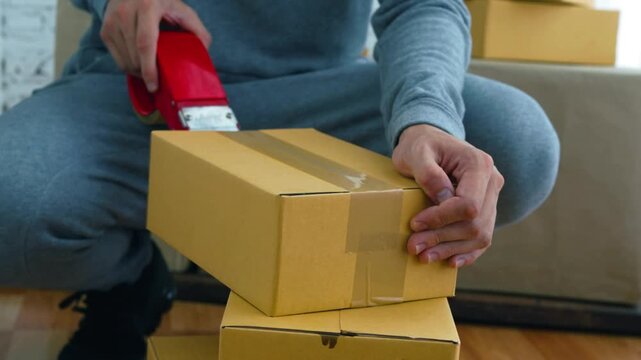 Young male warehouse worker packing cardboard boxes for shipment - relocation and logistics concept