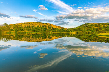 Naklejka premium Enchanted Rock's granite dome and surrounding oak-covered hills create a perfect mirror image in the glassy waters of Sandy Creek pond at sunset, Texas.
