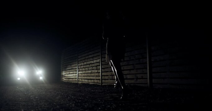 Silhouetted figure runs through a dark path illuminated by headlights during a late-night jog