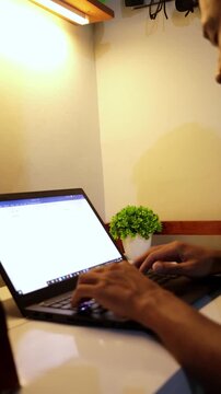close-up video of asian man typing on a laptop at a home workspace. This scene represents remote work, productivity, online communication, and modern digital lifestyle in a comfortable home office env