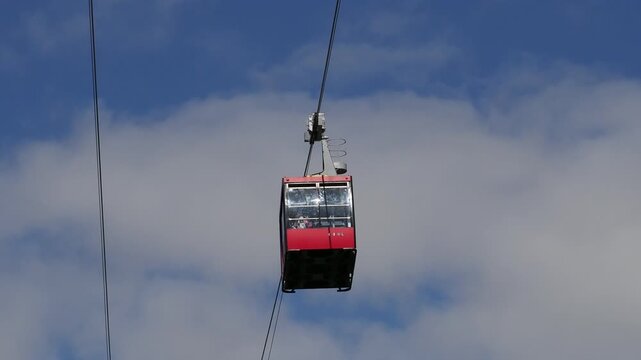 red funicular car leading to the top of the old mountain. The tourist car rides above rocky mountains dotted with cypress trees. Cable car cabins amazing sky and clouds. Cableway, green transportation