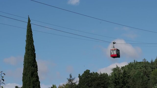 red funicular car leading to the top of the old mountain. The tourist car rides above rocky mountains dotted with cypress trees. Cable car cabins amazing sky and clouds. Cableway, green transportation