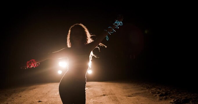 Girl dances in silhouette against car headlights on a dark country road at night, creating an ethereal atmosphere of freedom and joy