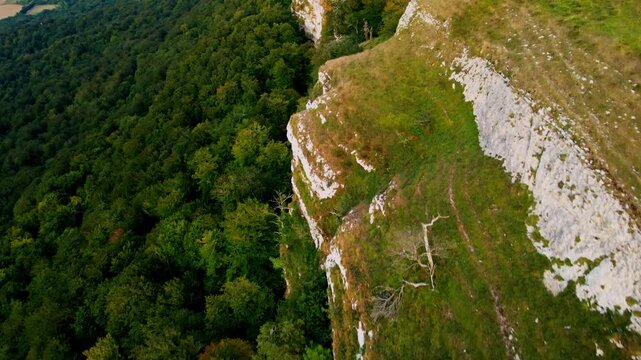 Cinematic drone flight over the mountain spine in Northern Spain. The footage captures a breathtaking perspective of steep rocky cliffs on one side and lush green forests on the other, overlooking a v