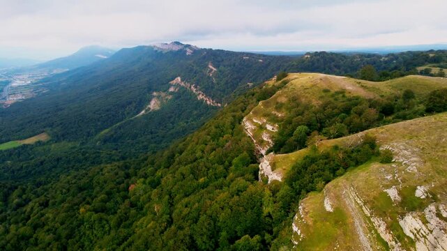Cinematic drone flight over the mountain spine in Northern Spain. The footage captures a breathtaking perspective of steep rocky cliffs on one side and lush green forests on the other, overlooking a v